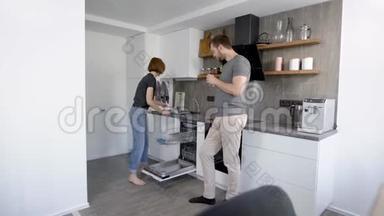 漂亮的一对夫妇用脏盘子、杯子和餐具装洗碗机。